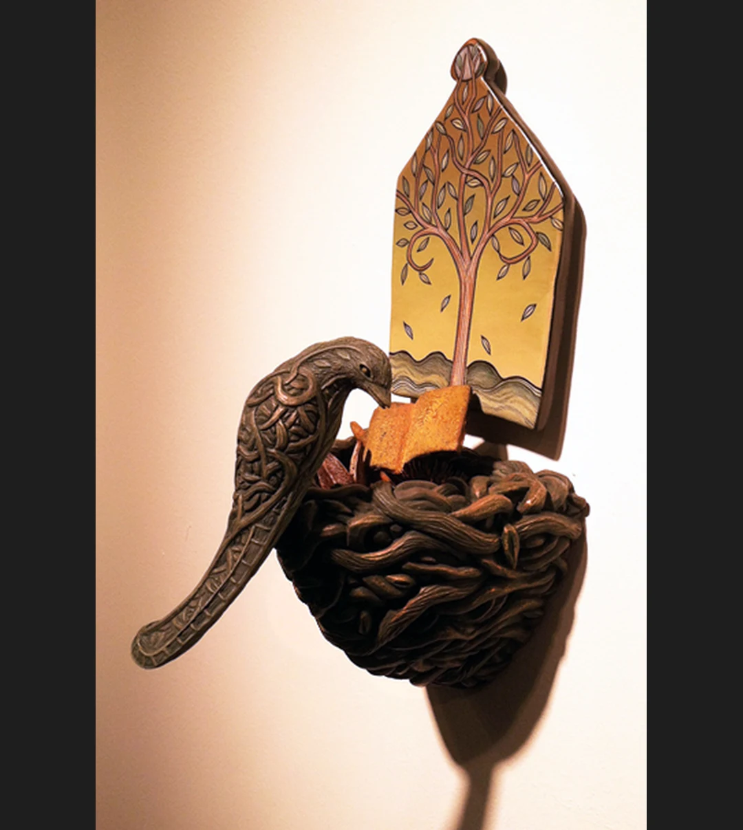 Ceramic wall sculpture of a bird perched on a nest, with a house-shaped tile painted with a tree mounted behind it.