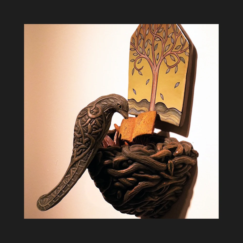 Ceramic wall sculpture of a bird perched on a nest, with a house-shaped tile painted with a tree mounted behind it.