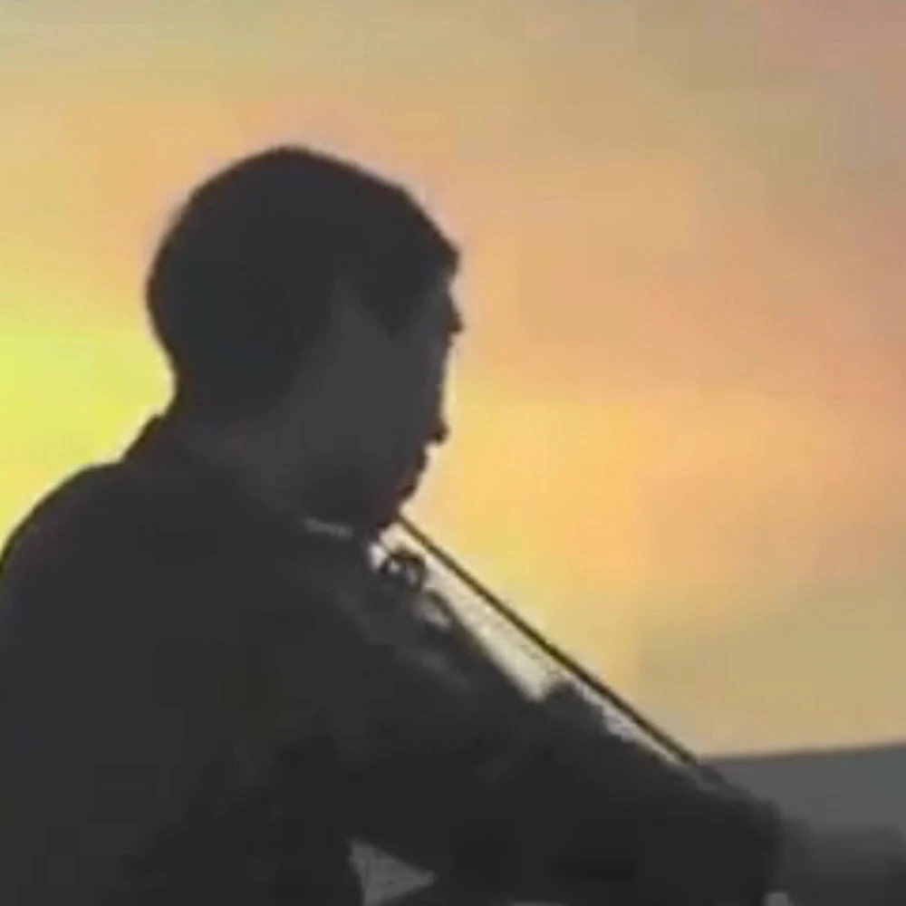 A violinist silhouetted in dark profile, playing against a glowing yellow-orange projected backdrop.