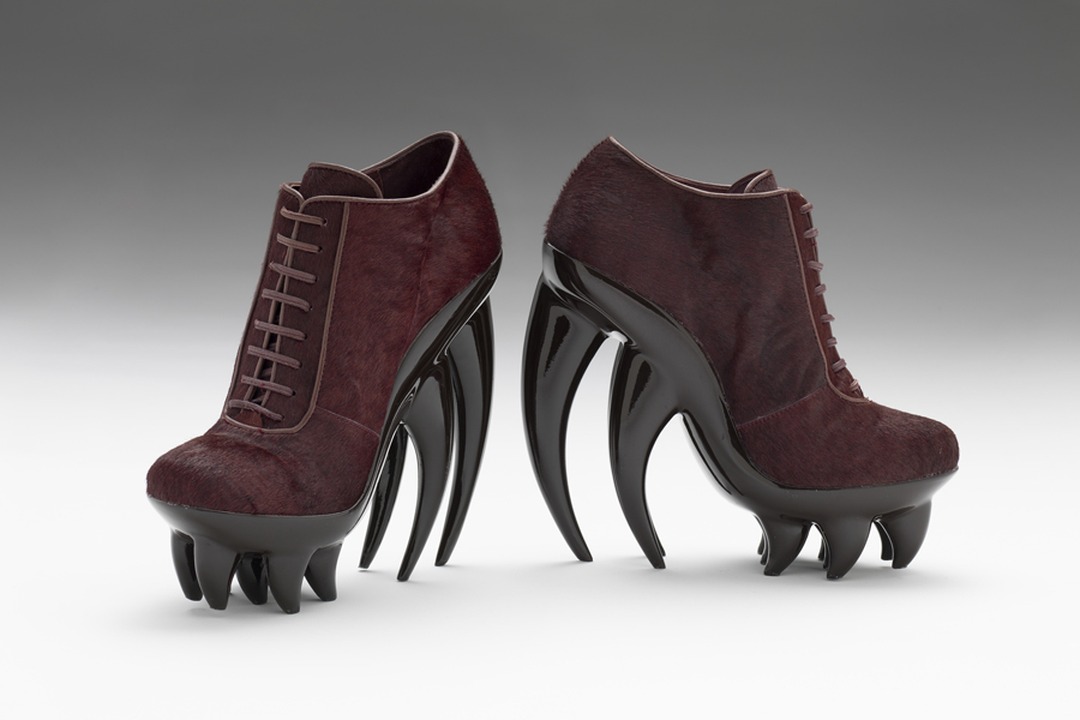 Iris van Herpen's Fang Shoes (2012): burgundy pony-fur lace-up boots with glossy black fang-shaped heels, photographed against a gray studio background.