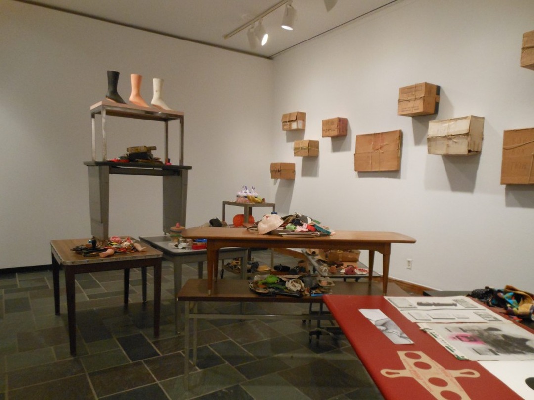 Installation view of the Bob Boxes exhibition: tables covered with small objects and wrapped packages, with cardboard boxes tied with string mounted on the gallery walls.
