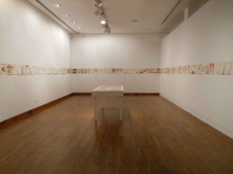 Installation view of Western Illinois University’s “Correspondence Show”: a frieze of mail-art works hung in a row along the gallery walls around a central vitrine. Photo: Cynthia Kukla.