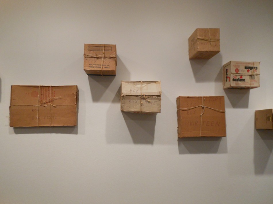 Six cardboard boxes tied with string, labeled “Bob Box Eight” and “Bob Box Thirteen”, mounted on a gallery wall. Photo: Cynthia Kukla.