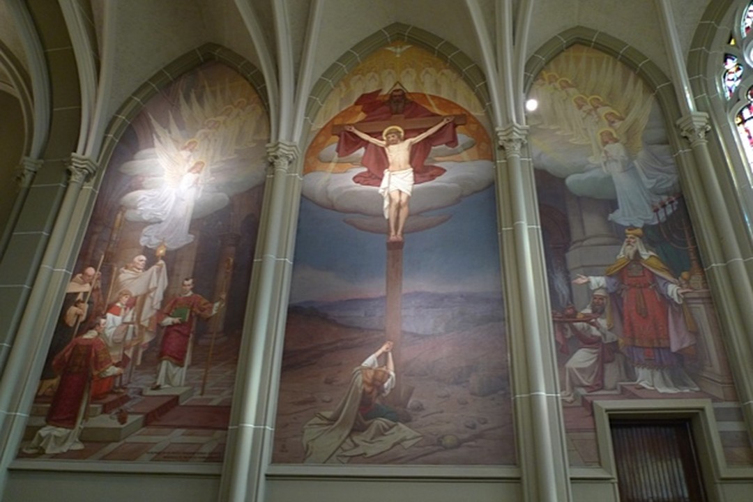 Wide view of Frank Duvenek's three murals in the Blessed Sacrament Chapel of St. Mary's Cathedral Basilica of the Assumption, Covington: Christ crucified in the central panel, flanked by a priest praying in a temple on the left and a priest with altar servers on the right.
