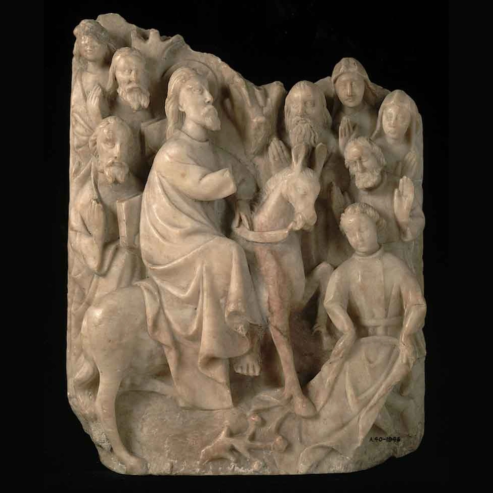 Pale alabaster relief of Christ riding a donkey into a crowd of onlookers, with a youth spreading a cloth on the ground in front.