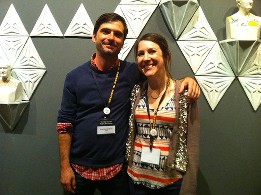 Katie Parker and Guy Michael Davis smiling side by side in front of a wall of white geometric pieces.