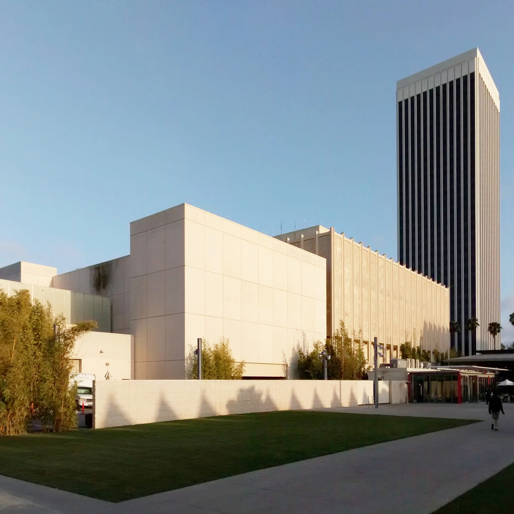 Exterior of the Los Angeles County Museum of Art: a pale stone-clad gallery block with a high-rise tower behind it, under a clear sky.