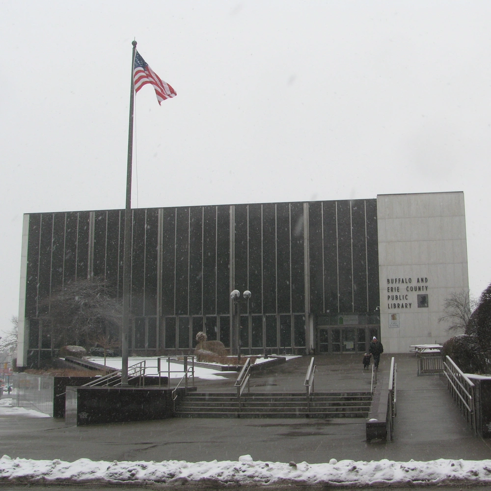 Exterior of the Buffalo and Erie County Public Library Central Library: a dark-clad modern building with a flag and steps in the snow.
