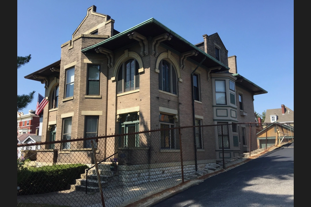 Brick Victorian building with arched stained-glass windows, a green copper roof edge and an American flag, on a hill in Clifton.