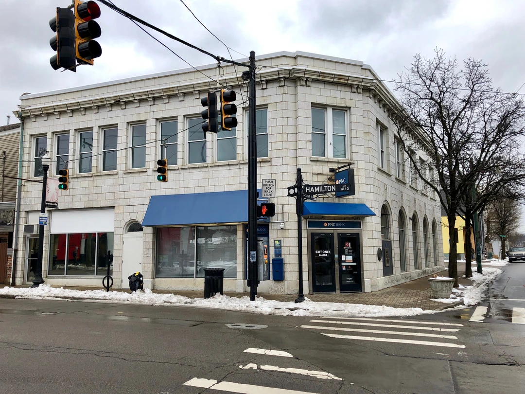 Corner storefront building with large windows and blue awnings on a Northside street, with traffic signals in front.