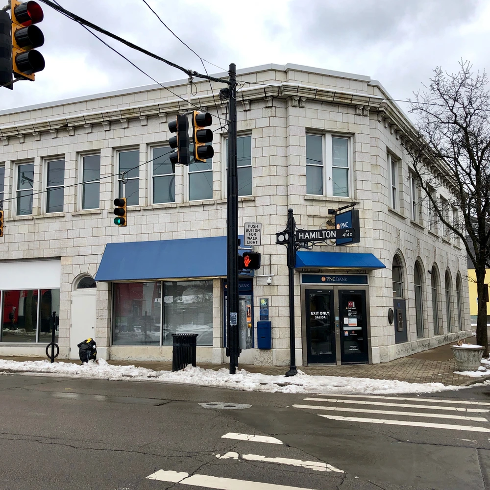 Corner storefront building with large windows and blue awnings on a Northside street, with traffic signals in front.