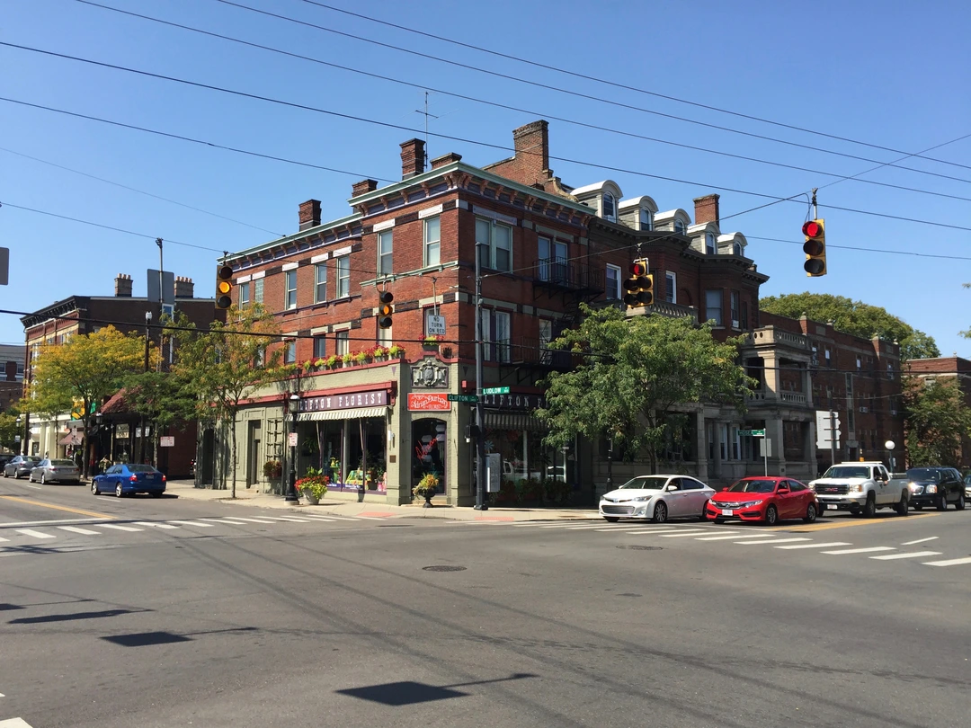 Red brick building with a green storefront and parked cars on a sunny street in the Clifton business district.