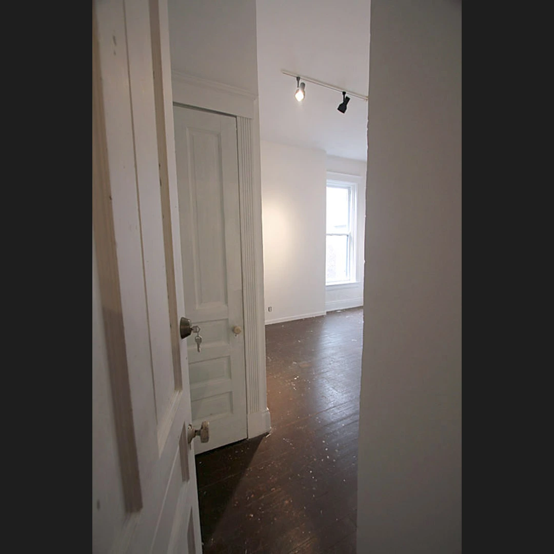 Empty studio room with a white door, a window on the back wall, and a dark wood floor.