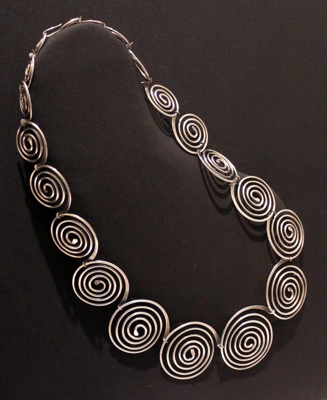 Necklace made of linked spiral shapes, displayed against a black background.