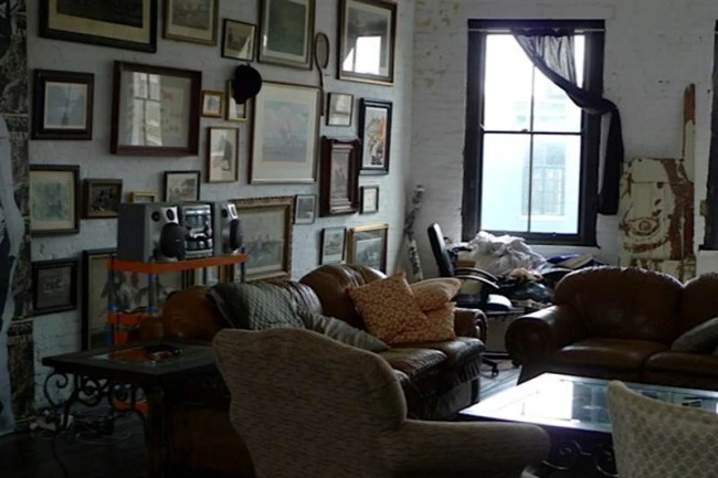 Lounge with leather couches and armchairs under a wall of framed pictures hung salon style, with a stereo unit and a window.