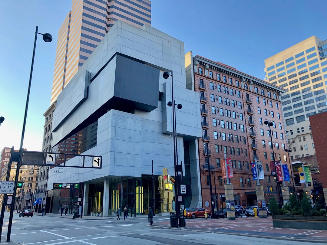 Exterior of the Contemporary Arts Center in Cincinnati: a white stone building with a dark box overhanging the sidewalk, beside a brick hotel and a tall office tower under a blue sky.