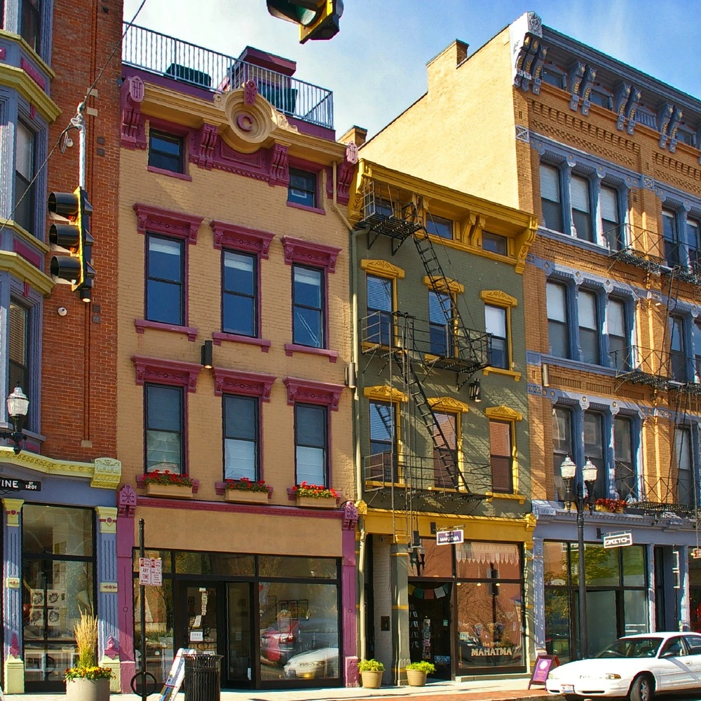 Restored brick and painted facades with bay windows and storefronts along a street in Over-the-Rhine, Cincinnati, under a blue sky.