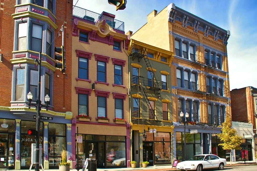 Restored brick and painted facades with bay windows and storefronts along a street in Over-the-Rhine, Cincinnati, under a blue sky.