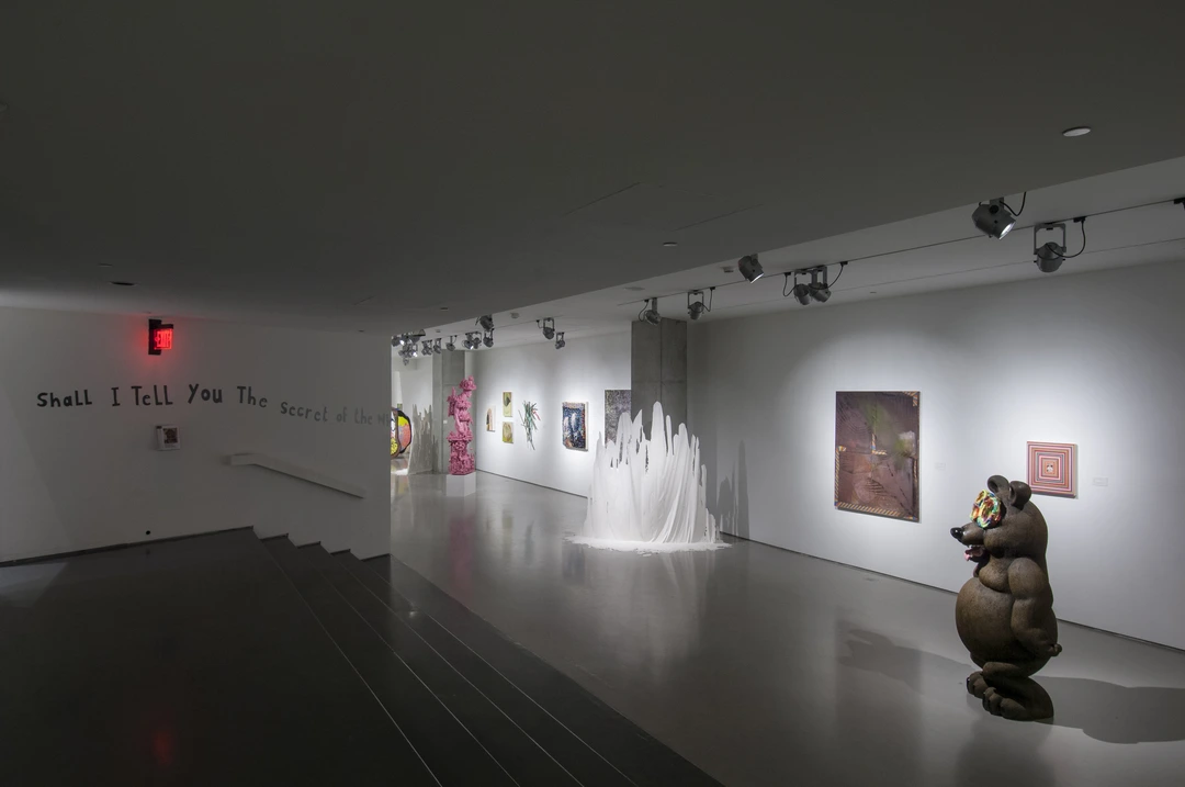 Entrance to a gallery with a wall text reading “Shall I tell you the...”, a large brown bear sculpture, and paintings on white walls.
