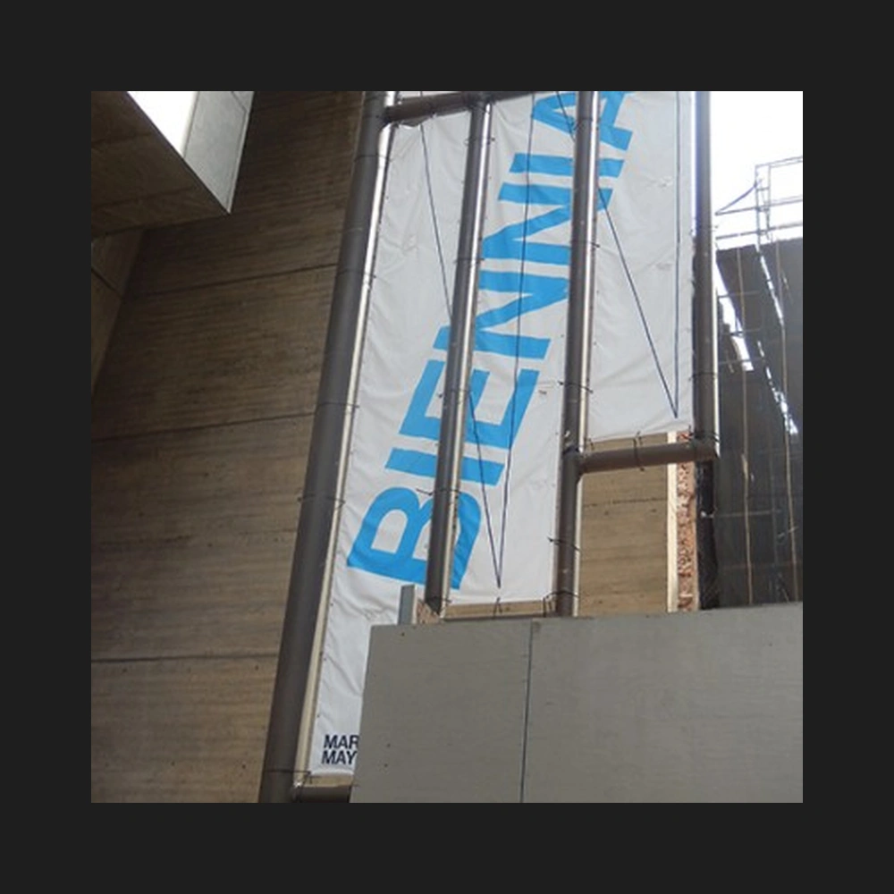 Blue Biennial banner hanging on a concrete museum facade, with scaffolding at right.