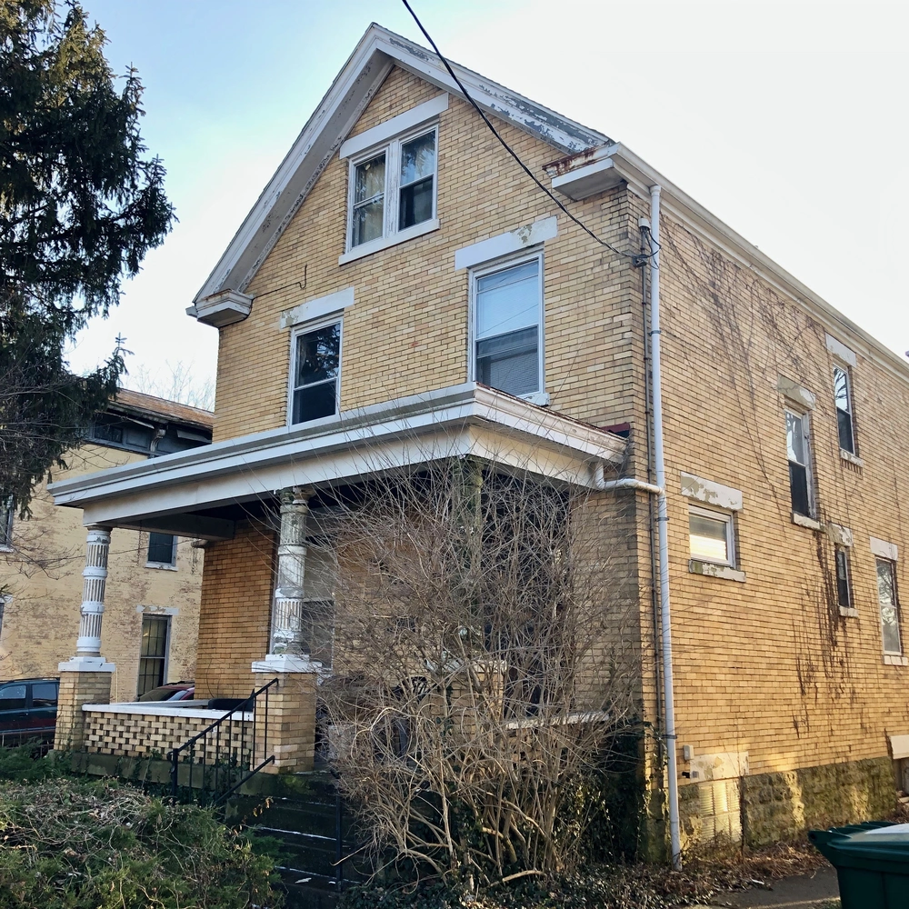 Yellow-brick two-story house with a front porch and a bare tree, on a Northside street.