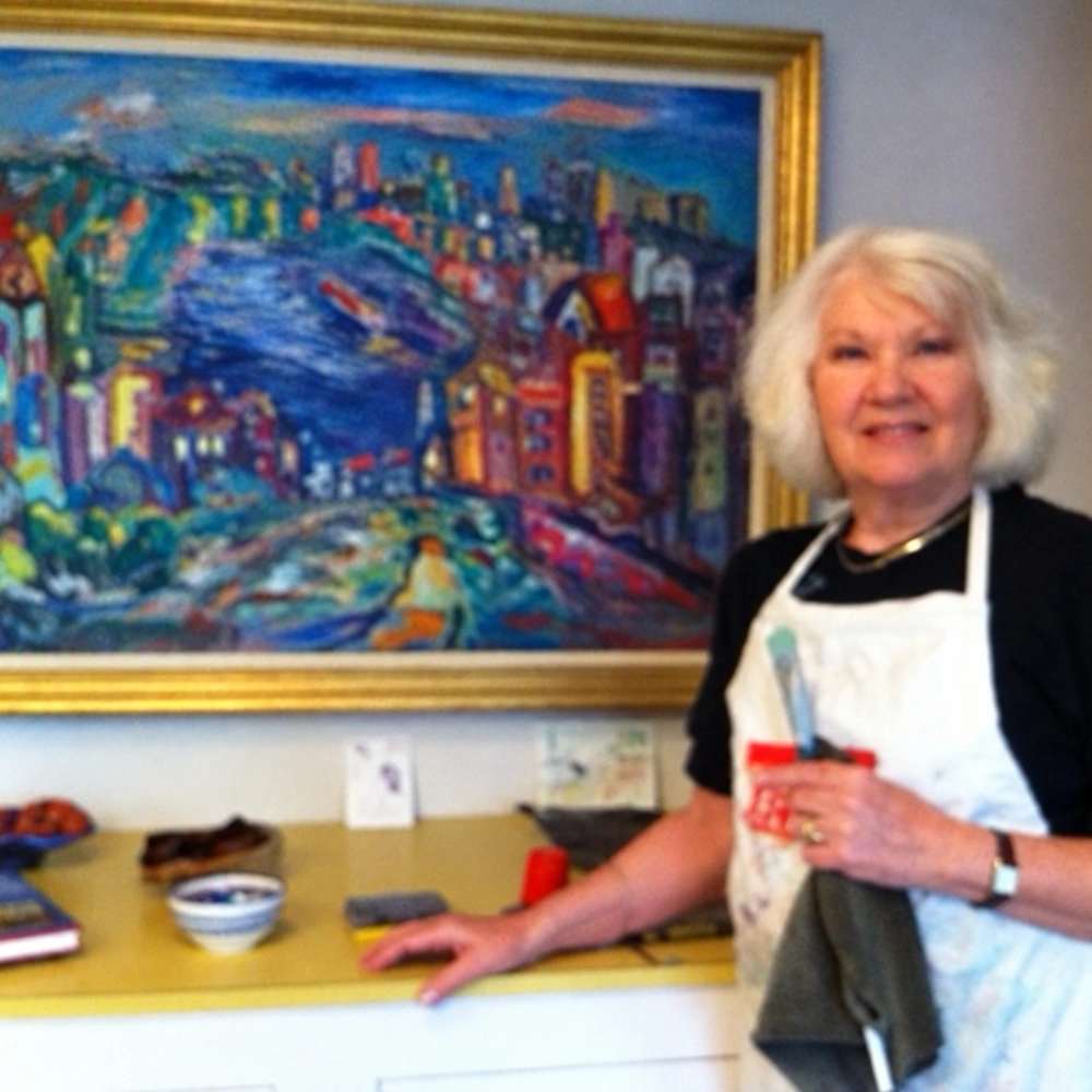 Square crop of a smiling white-haired woman beside a large gold-framed painting of a colourful city skyline.