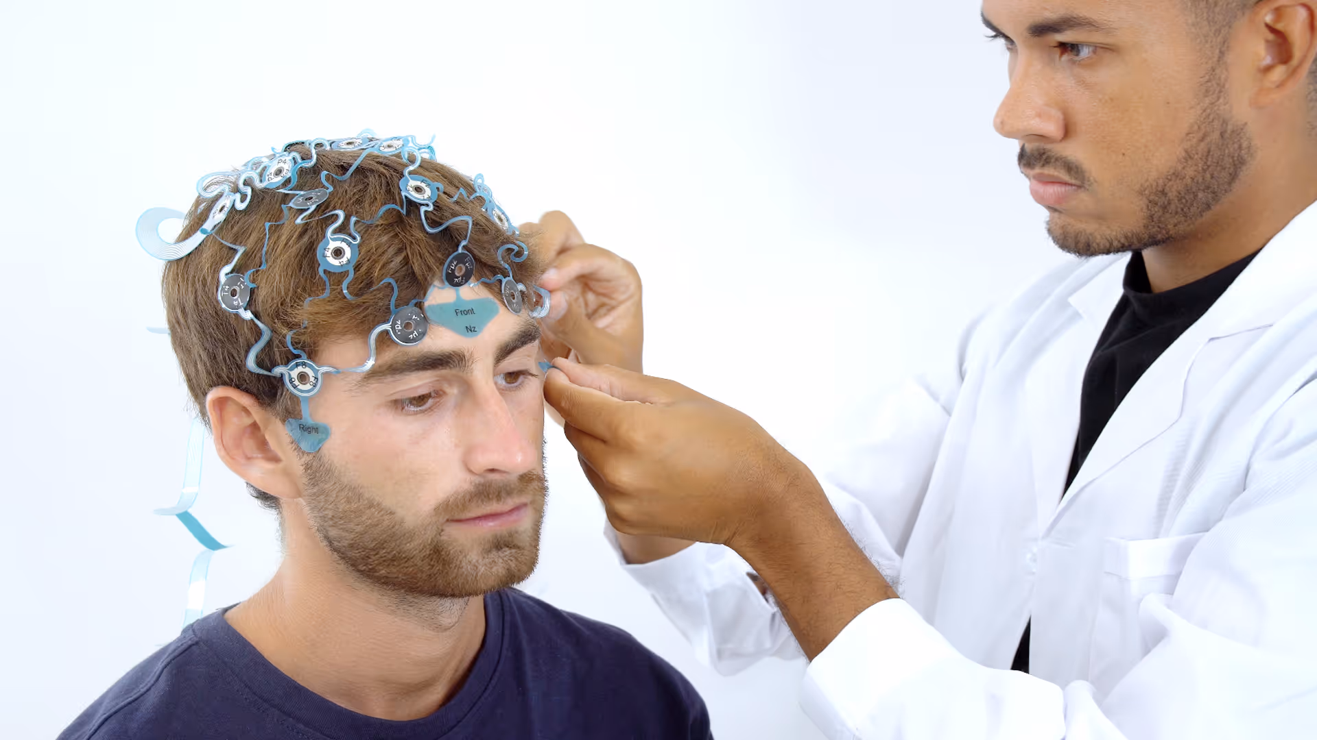 Technician fitting a head electrode cap with sensors on a man's head.