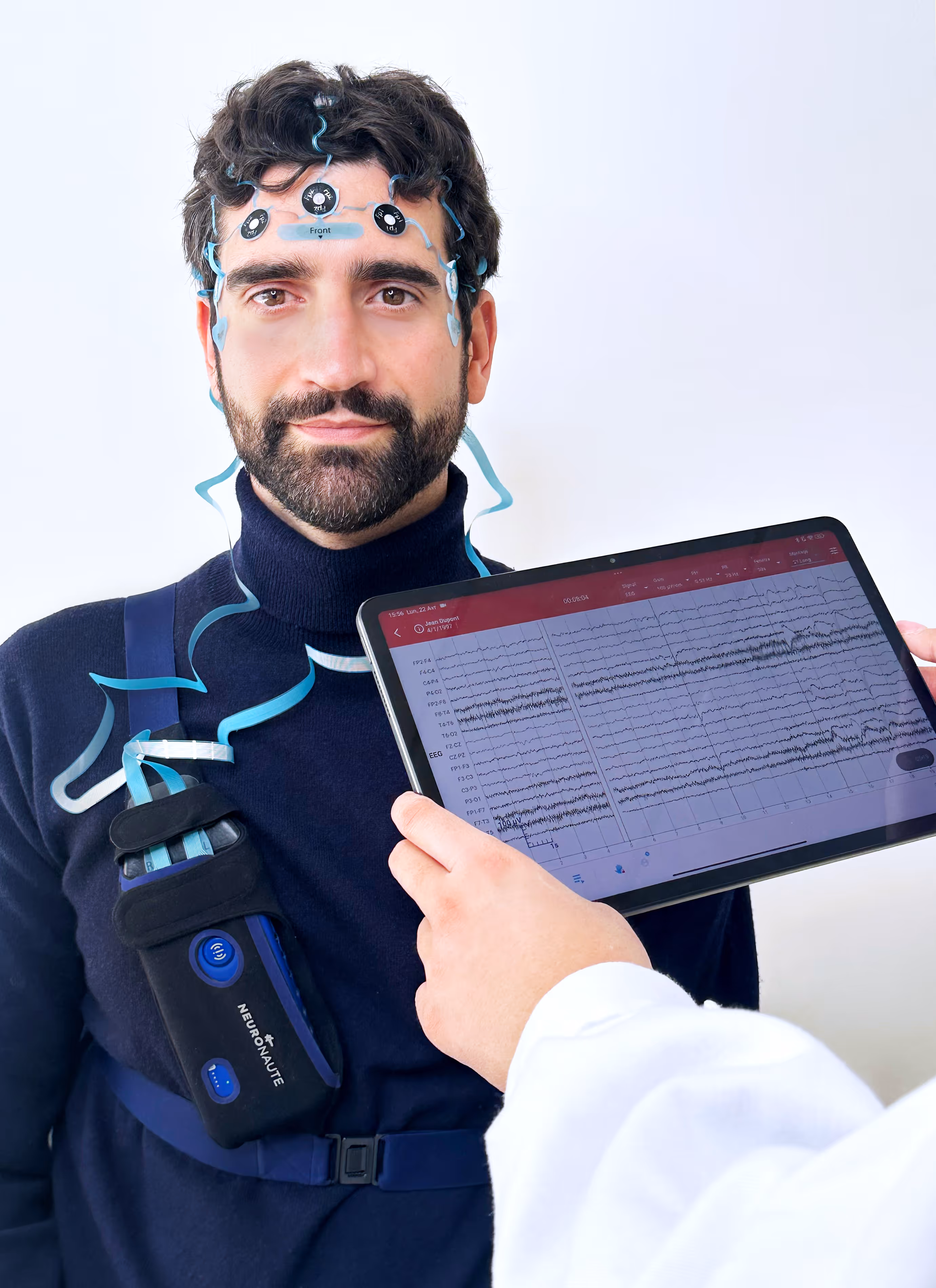 Man wearing a portable EEG device with electrodes on his forehead while a person in a white coat holds a tablet displaying brainwave patterns.