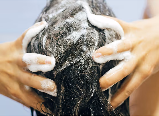 Hands massaging shampoo foam into wet dark hair.