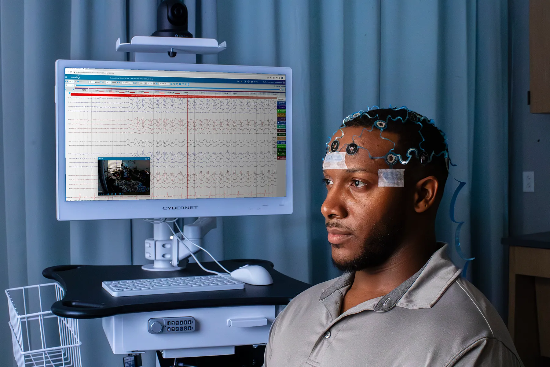 Man wearing EEG electrodes on his head, seated near a monitor displaying brainwave data.