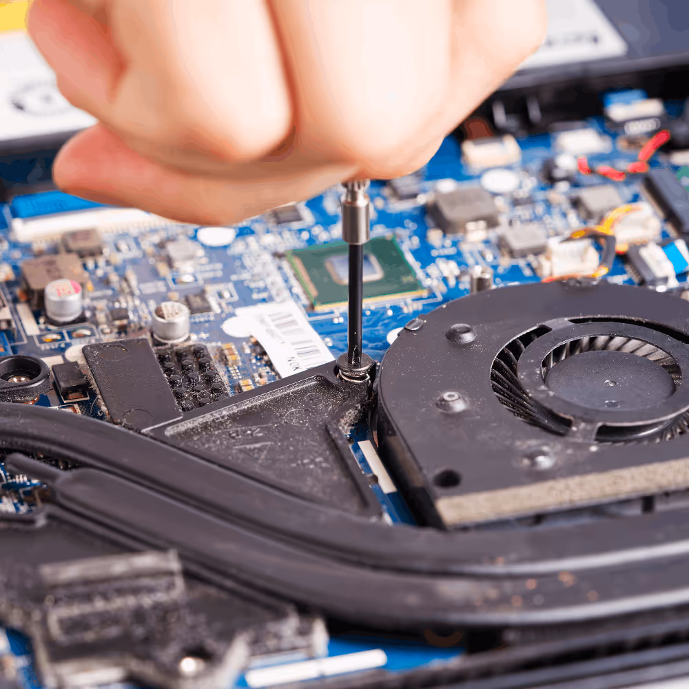 Hand using a screwdriver to repair a computer's internal hardware near the cooling fan.