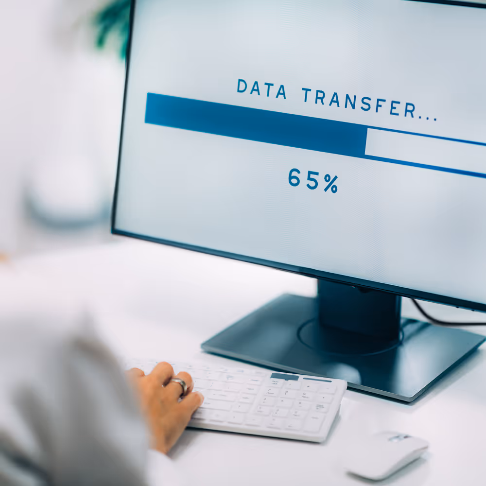Computer screen showing a data transfer progress bar at 65%, with a hand typing on a white keyboard below.