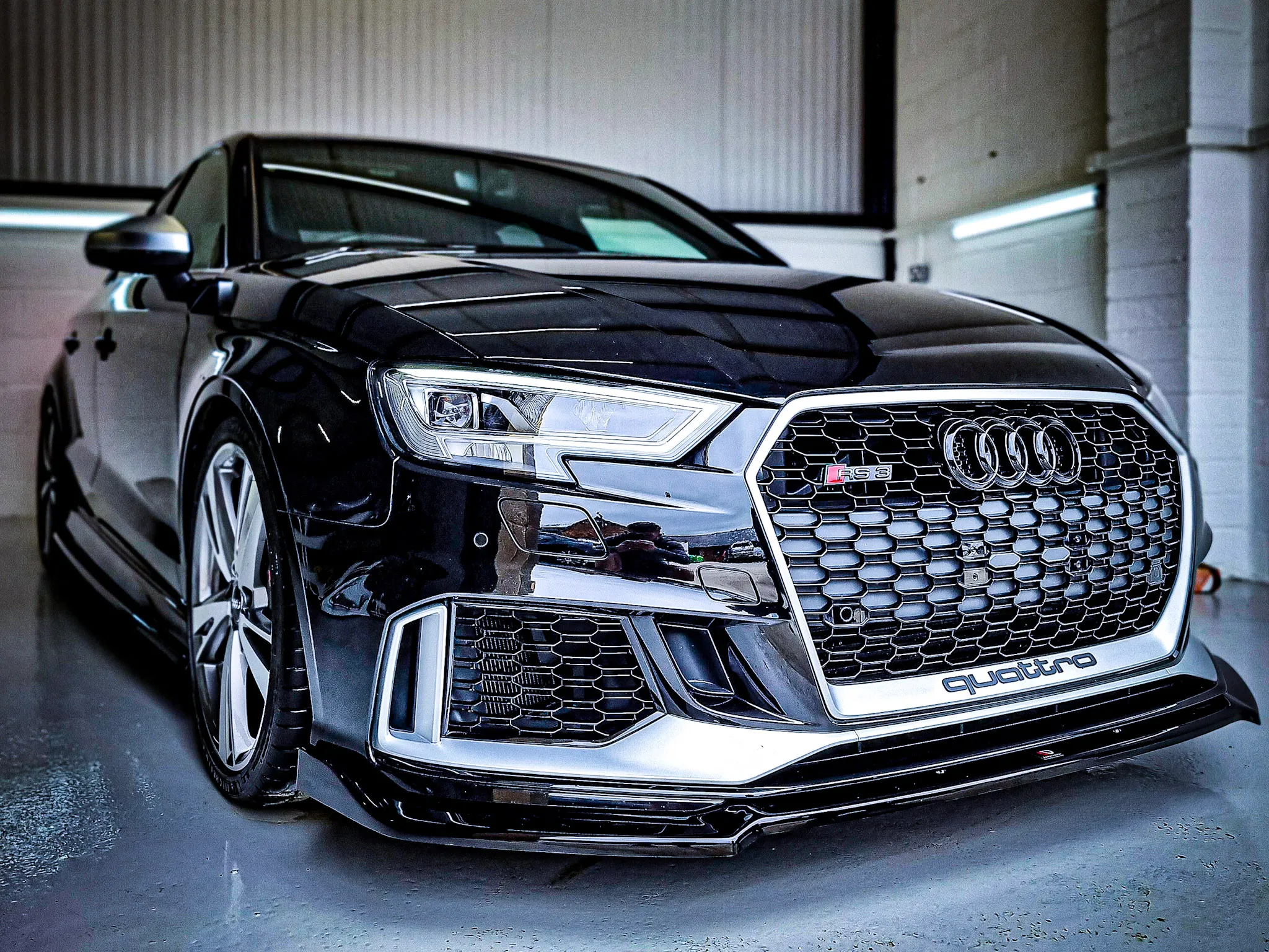 Black Audi RS3 parked indoors showing front grille with quattro badge and sleek headlights.