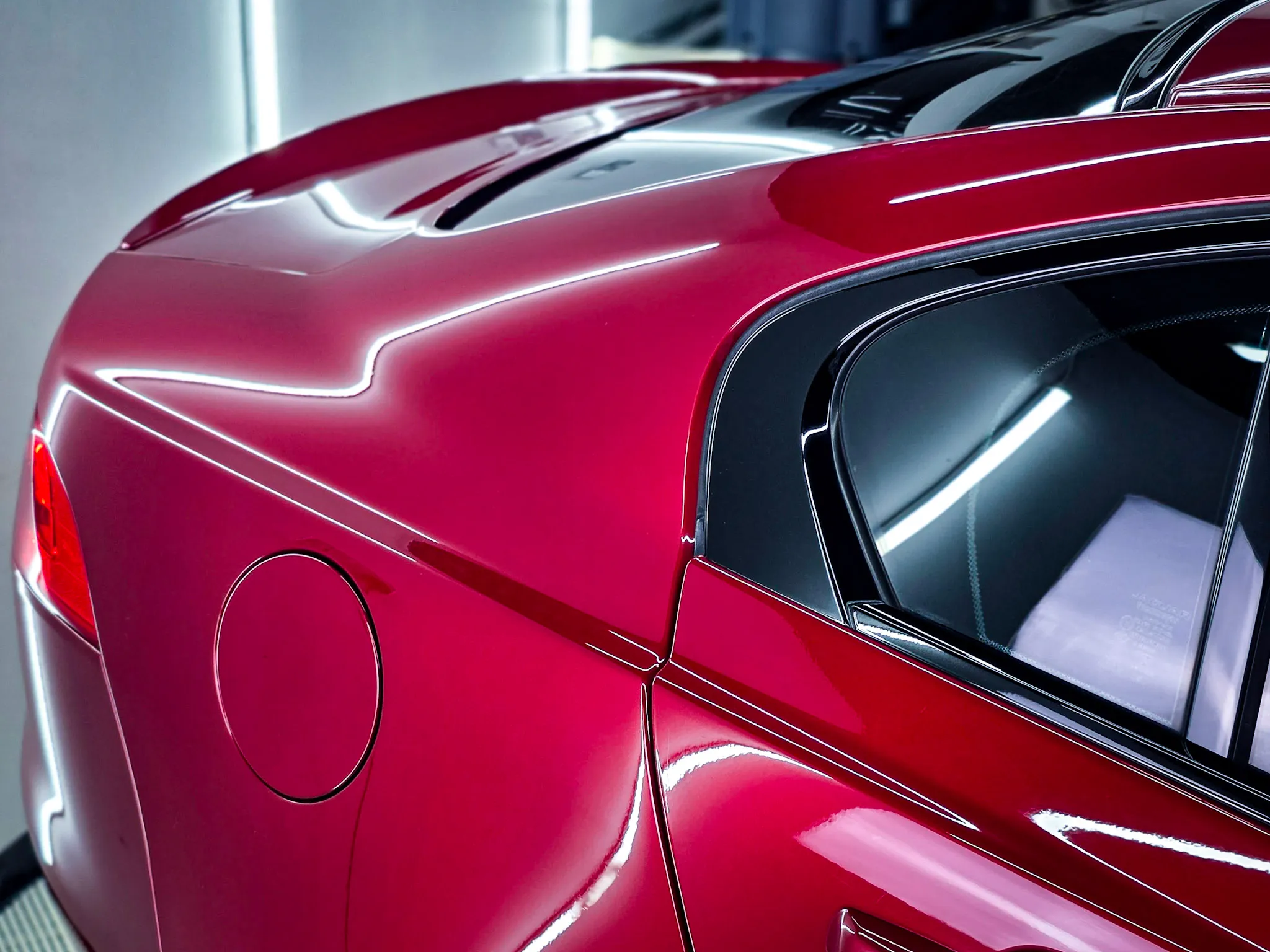 Close-up of the rear quarter panel of a shiny red car, showing the fuel cap, window, and sleek body lines.
