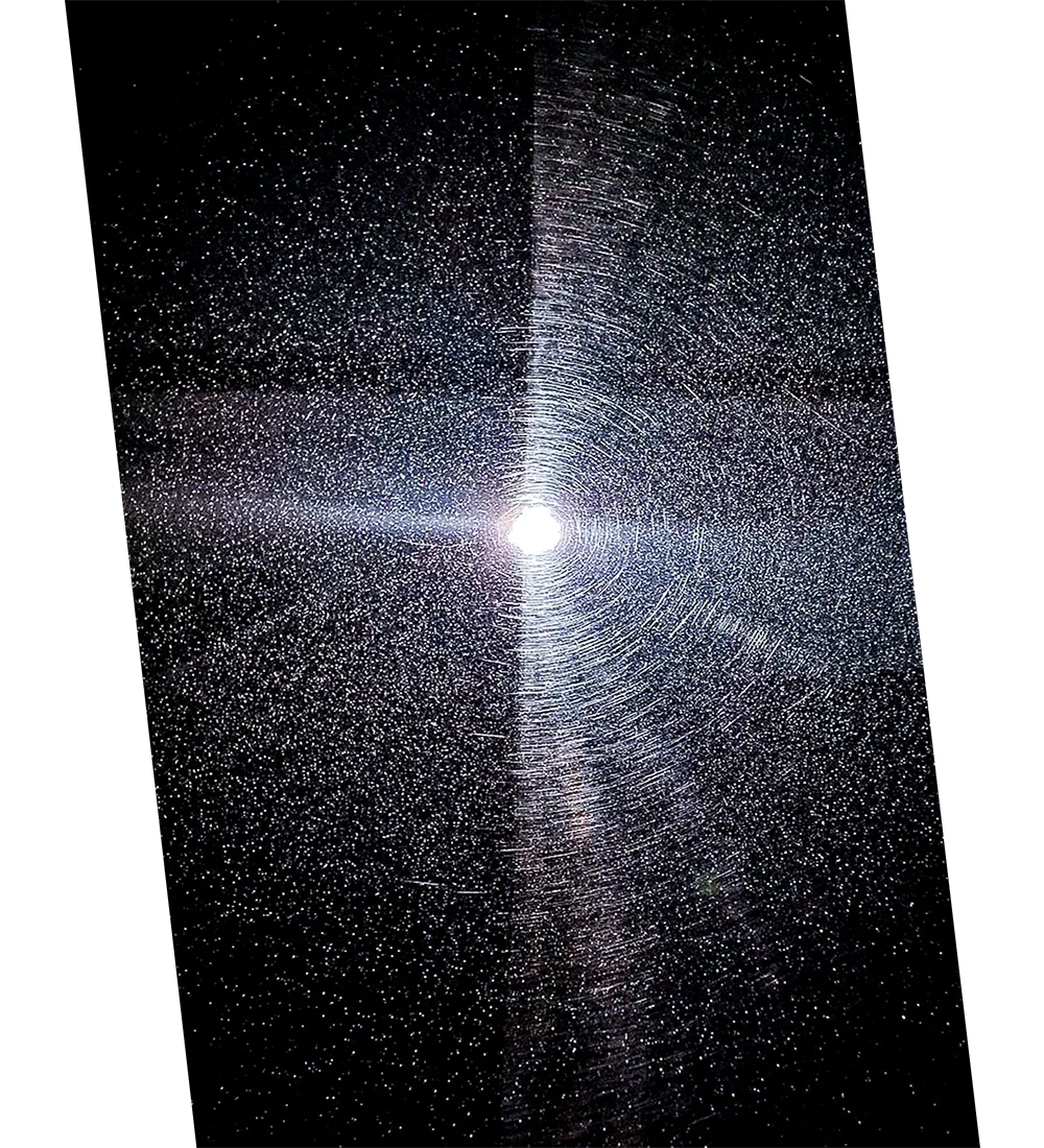 Close-up of a dark surface with numerous fine scratches and swirl marks reflecting light from a bright central source.