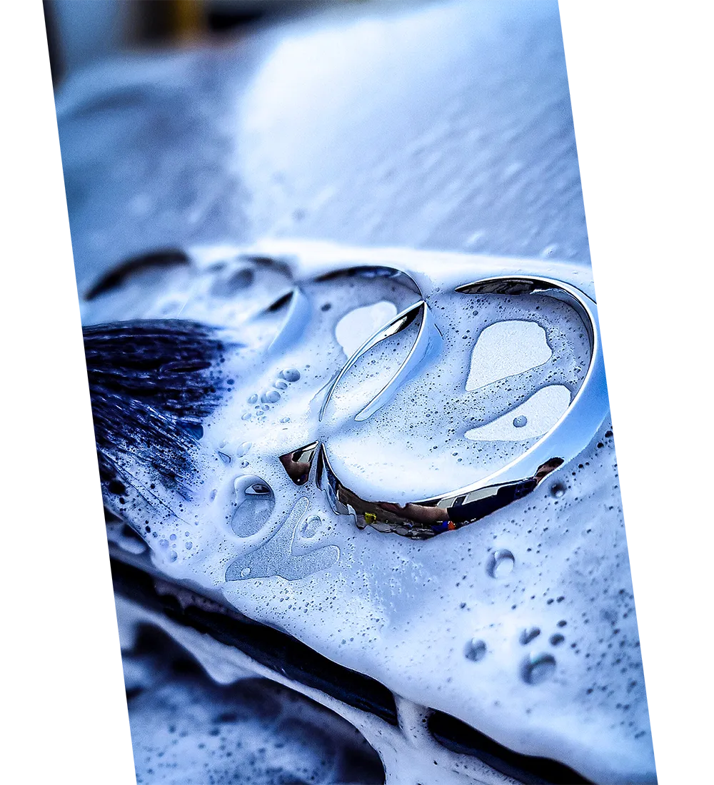 Close-up of a car emblem covered in blue soap suds during washing.