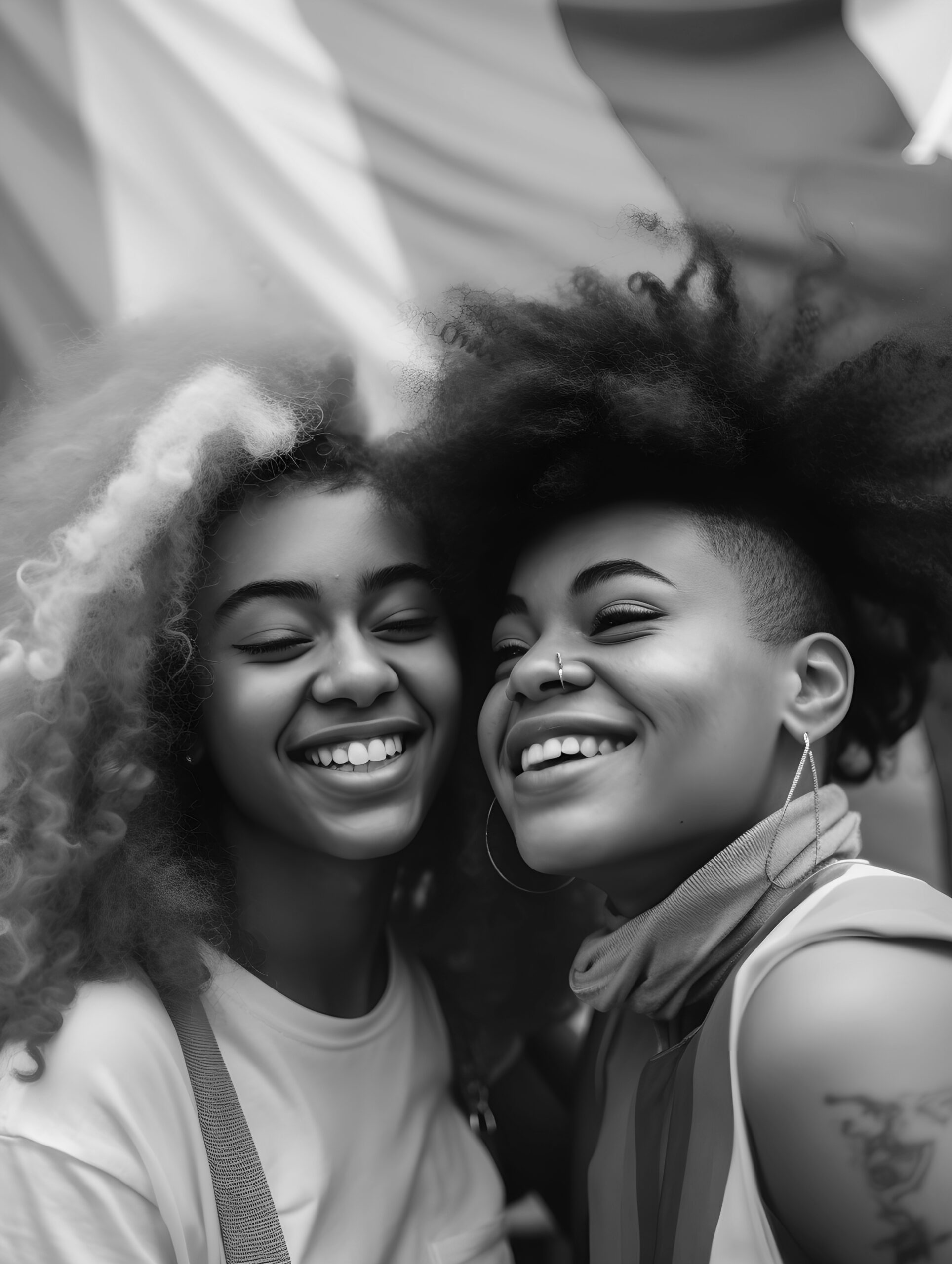 Two joyful people with natural curly hair smiling and hugging closely.