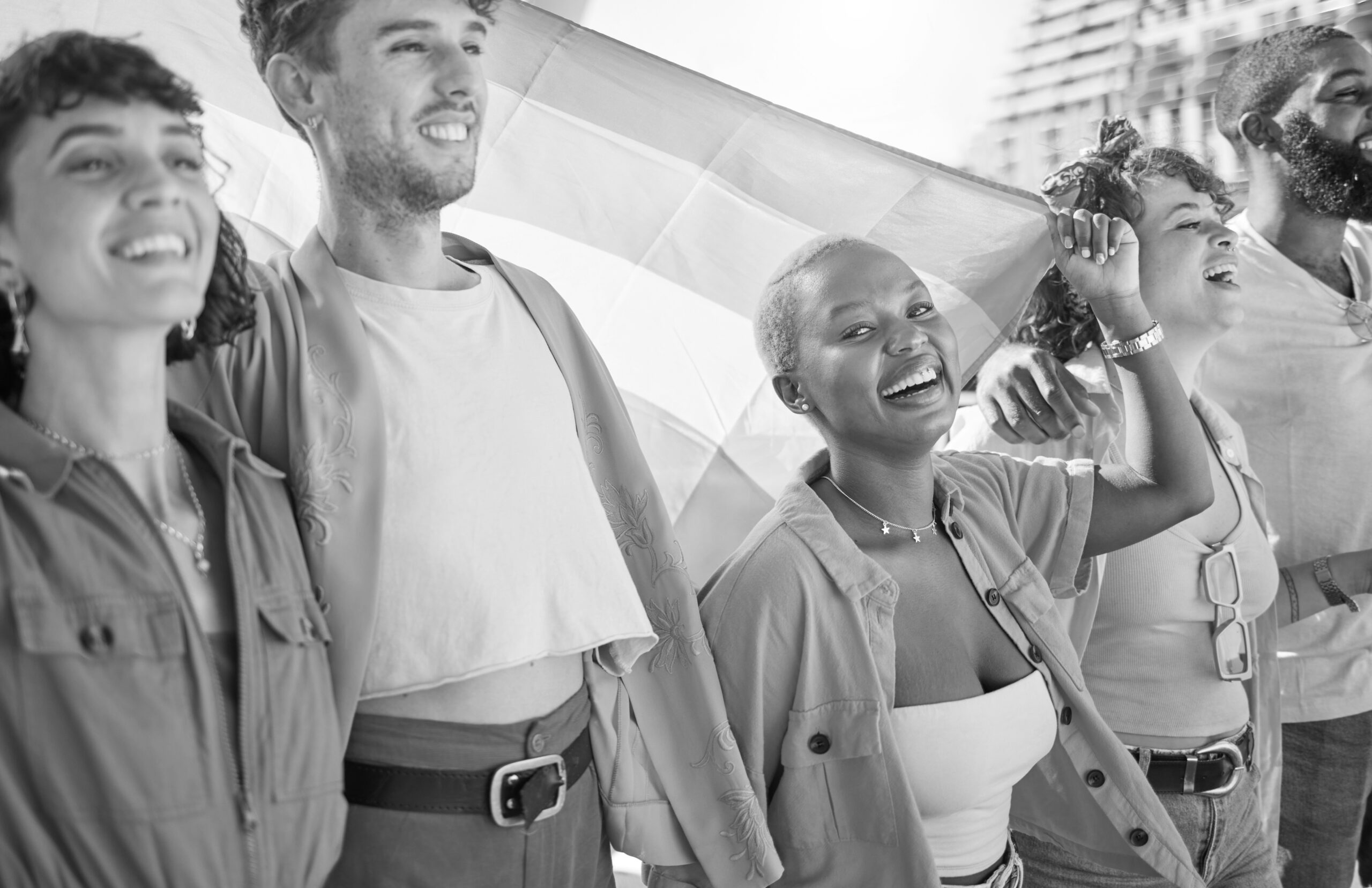 Diverse group of smiling young people standing together with a pride flag behind them.
