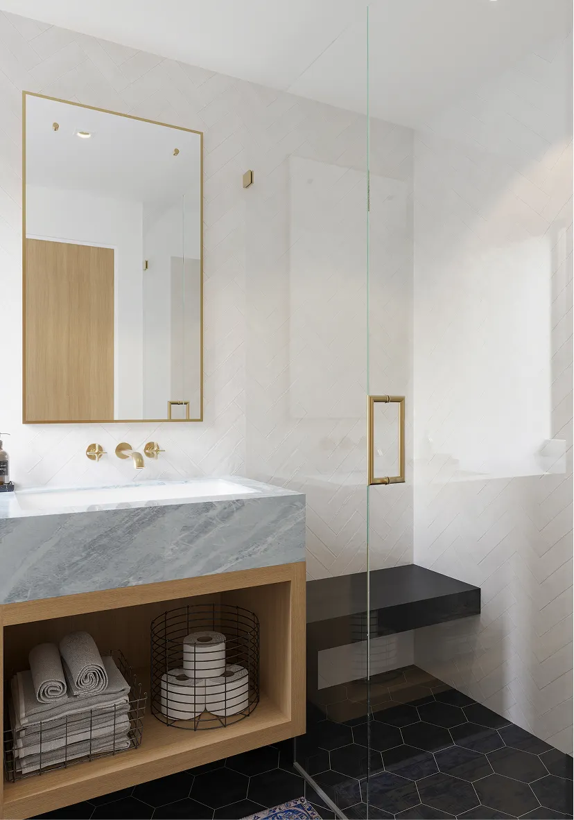 Modern bathroom with marble countertop sink, gold fixtures, wooden storage with towels and toilet paper, and glass shower enclosure with black hexagonal floor tiles.