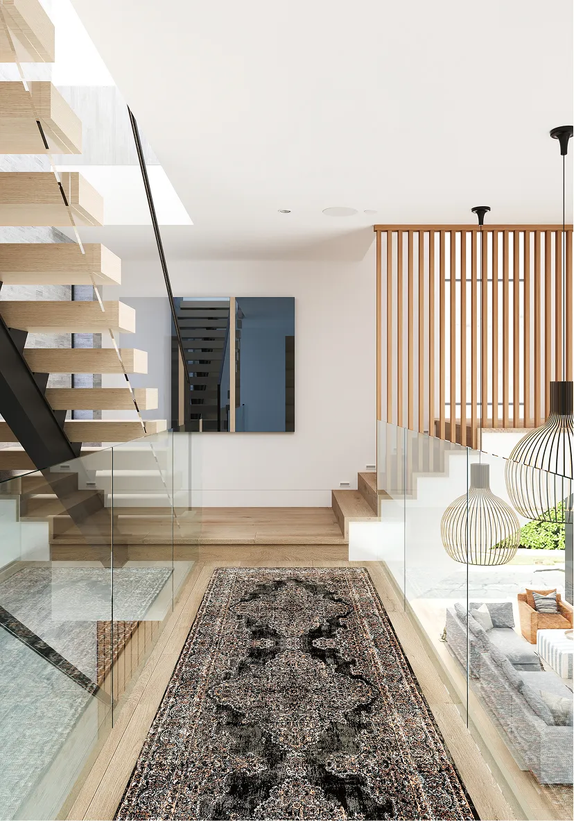 Modern interior hallway with floating wooden stairs, glass railings, and a patterned black and beige rug on light wood flooring.