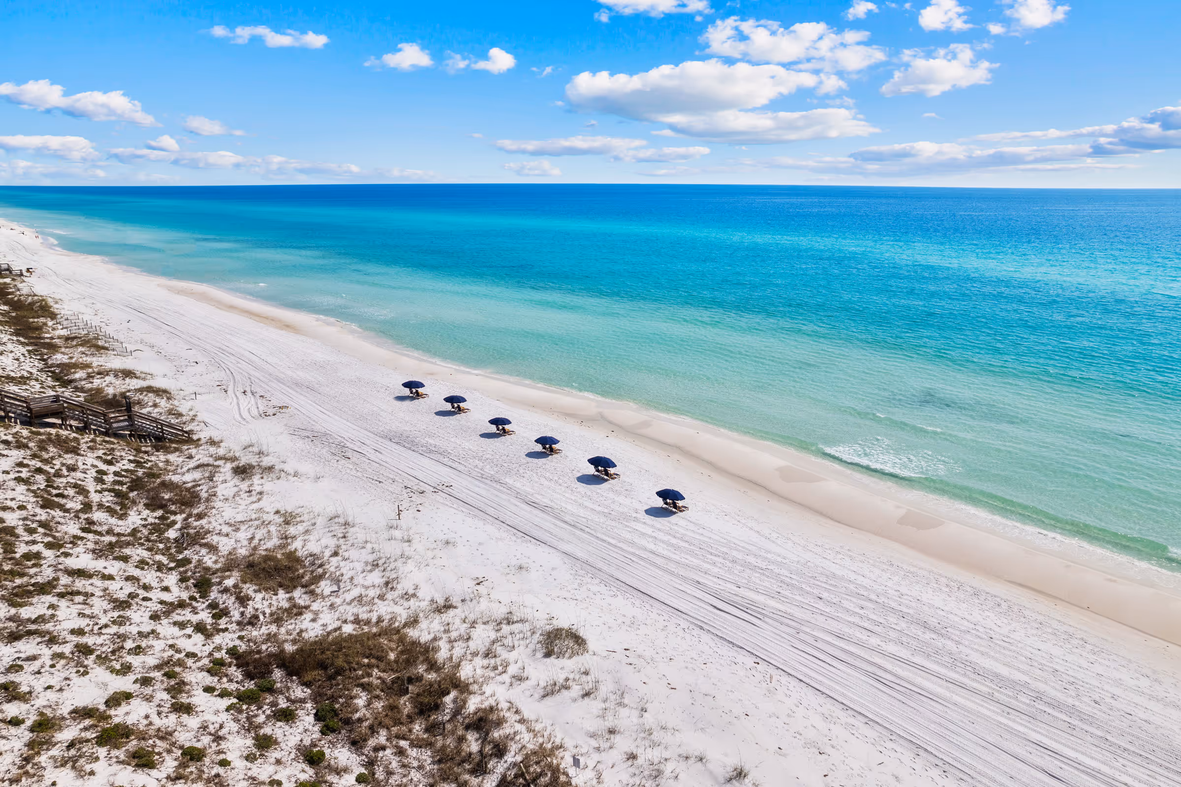 Scenic Florida shoreline with white sand, clear water, and shaded beach chairs