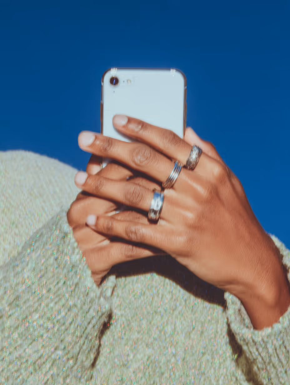 Hände mit mehreren Ringen, die ein weißes Smartphone vor blauem Hintergrund halten.