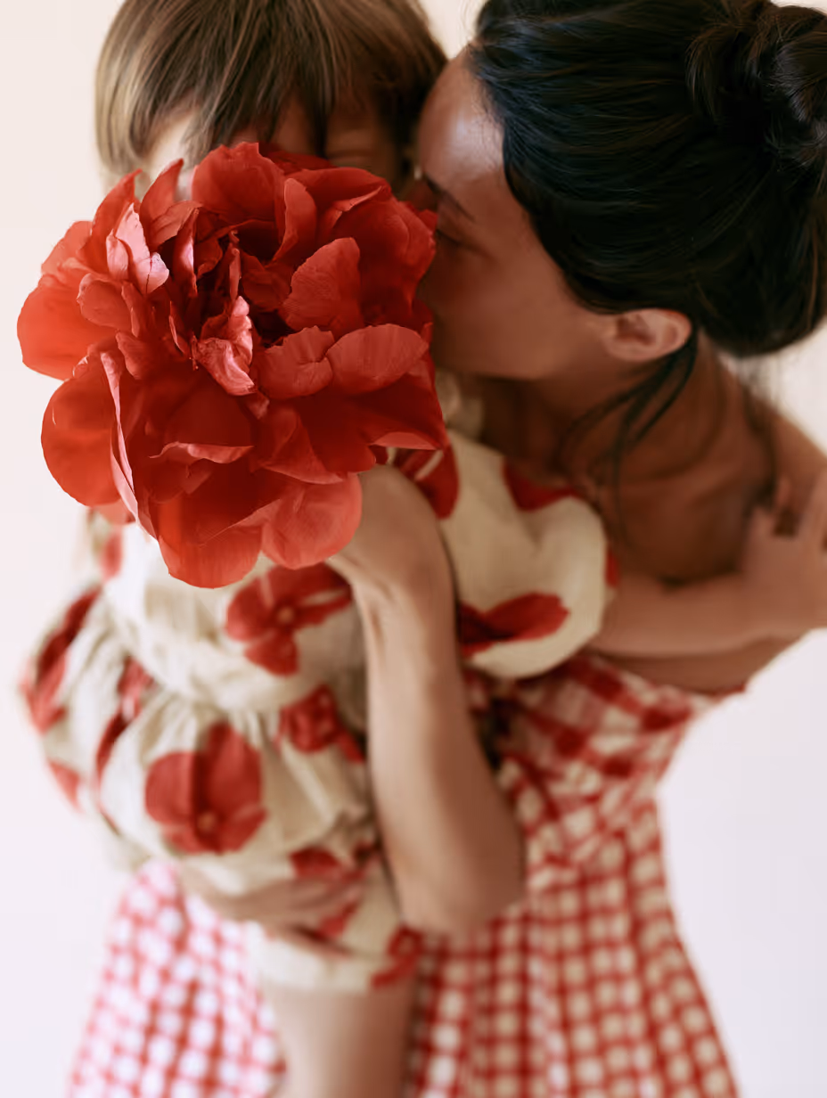 Eine Frau hält ein Kind, das eine rote Blume vor das Gesicht hält.