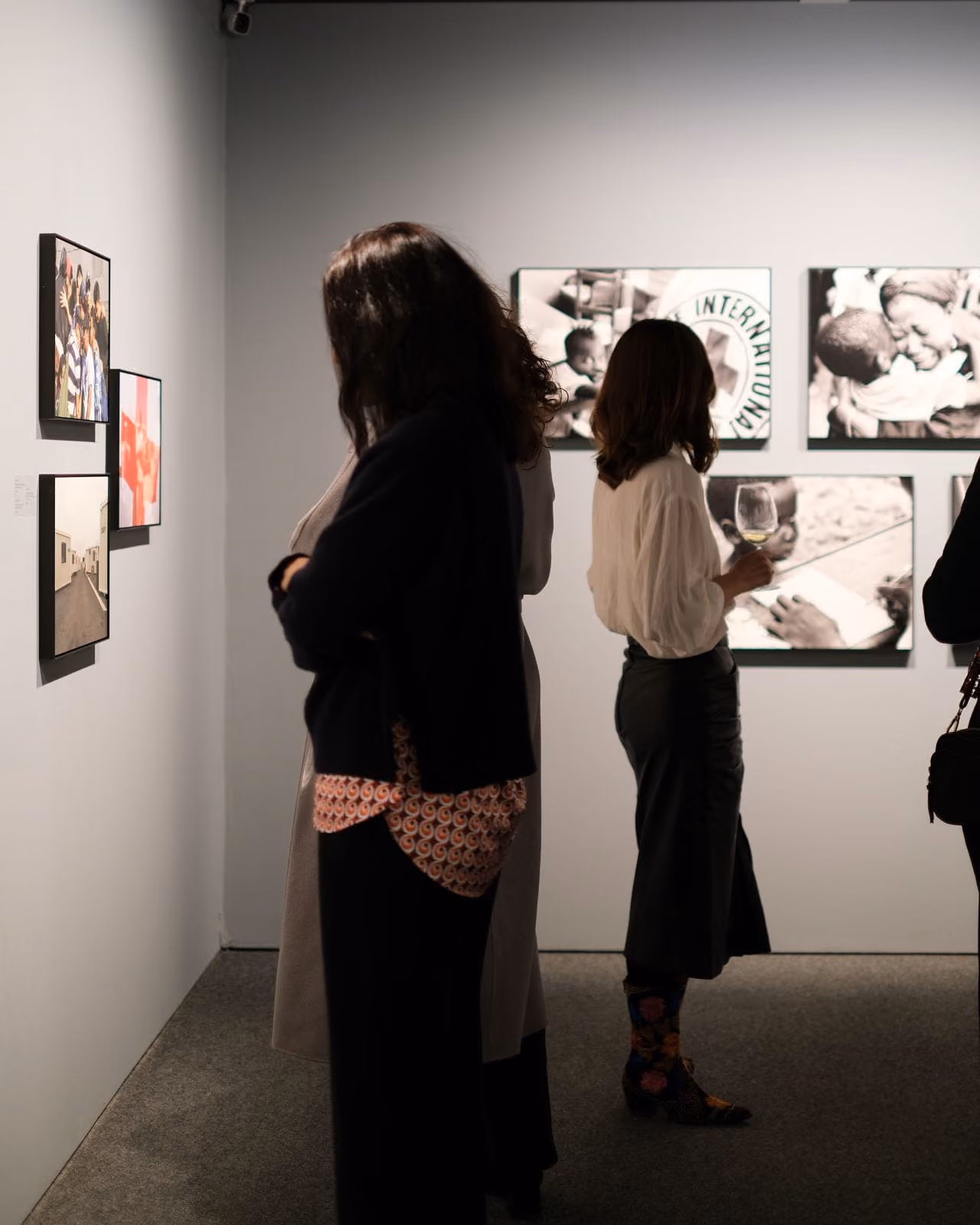 Menschen betrachten Fotografien in einer Galerie mit Schwarz-Weiß- und Farbbildern an den Wänden.