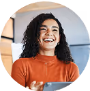 Lachende Frau mit Tablet in modernem Büro, trägt orangen Pullover.