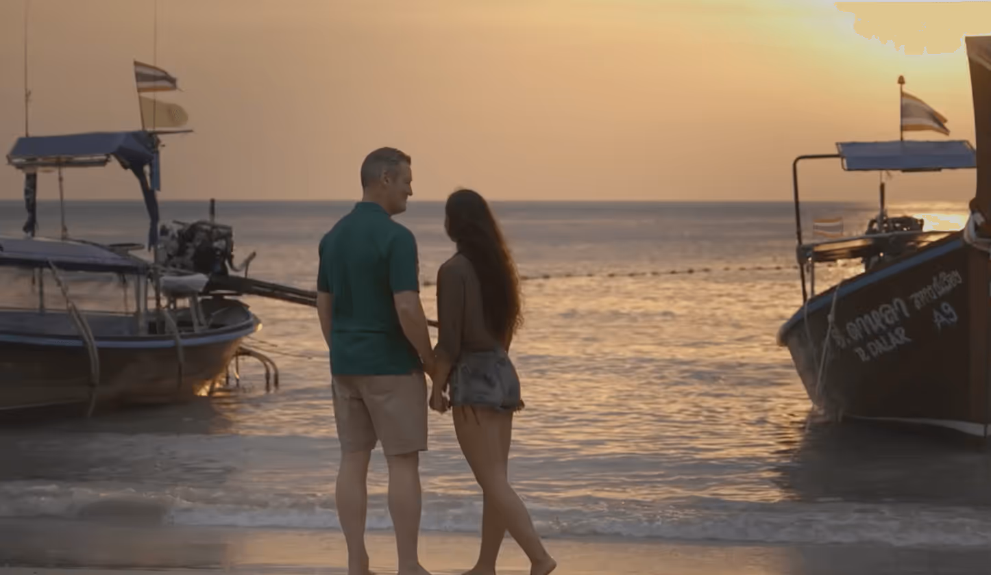 Paar am Strand bei Sonnenuntergang, umgeben von Fischerbooten, hält sich an den Händen und genießt die friedliche Atmosphäre.