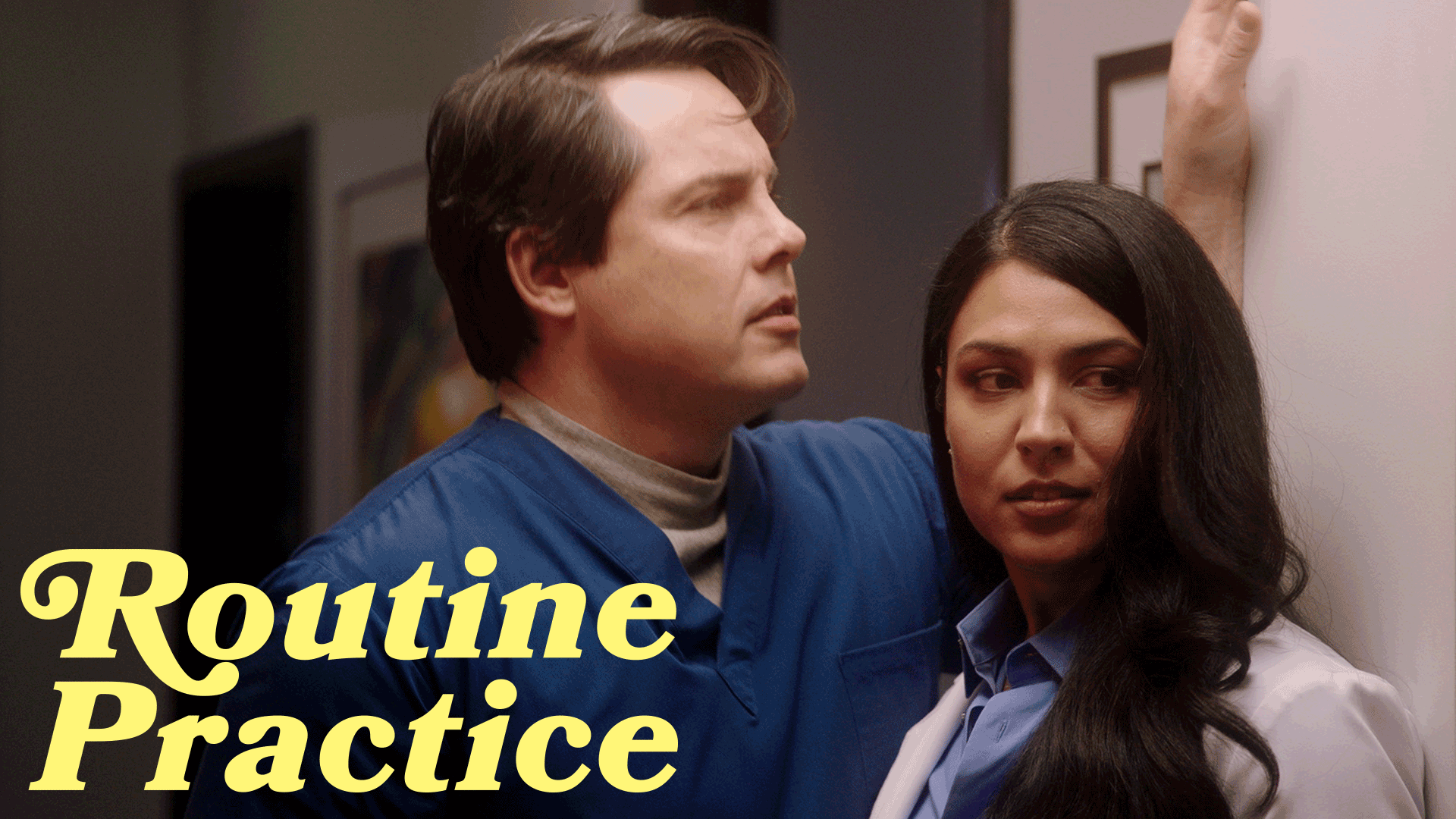 Man in blue scrubs leaning on a wall next to a woman in a white coat looking sideways, with the text 'Routine Practice' in yellow.
