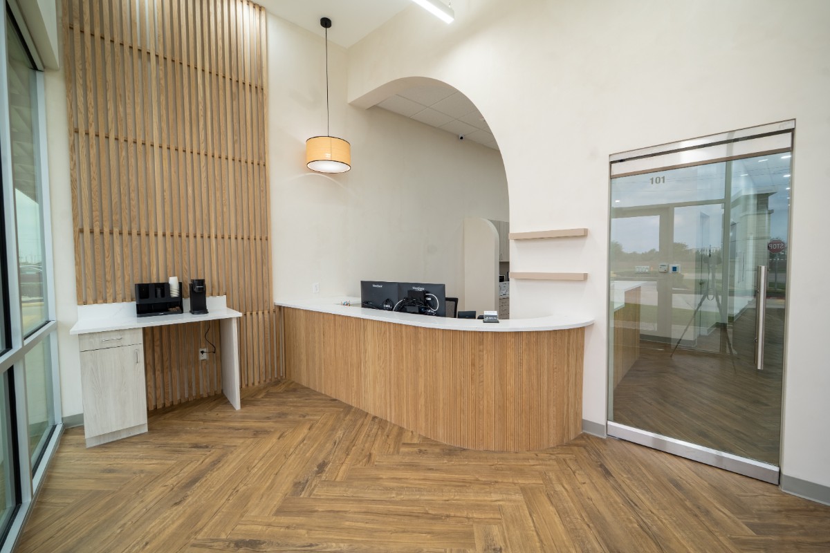 Modern office reception area with wooden counter, hanging light fixture, coffee station, and glass door labeled 101.