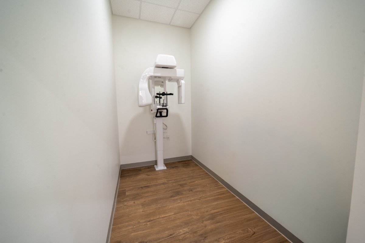 White dental panoramic X-ray machine in a small room with wood floor and white walls.