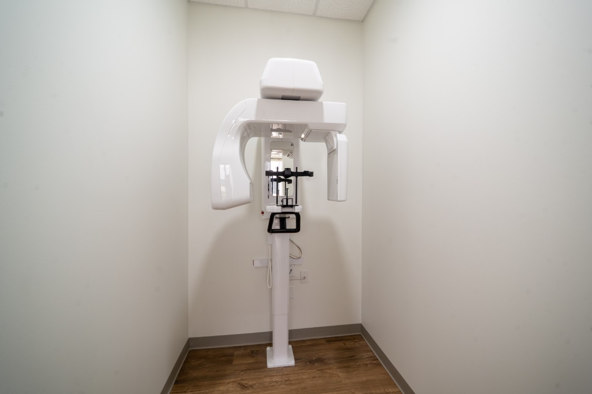 White dental panoramic X-ray machine mounted in a small room with white walls and wooden flooring.
